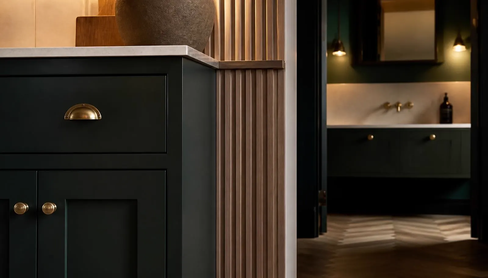 Bespoke dark-green shaker cabinetry with brass cup handles and fluted timber panelling beside a fitted bathroom vanity